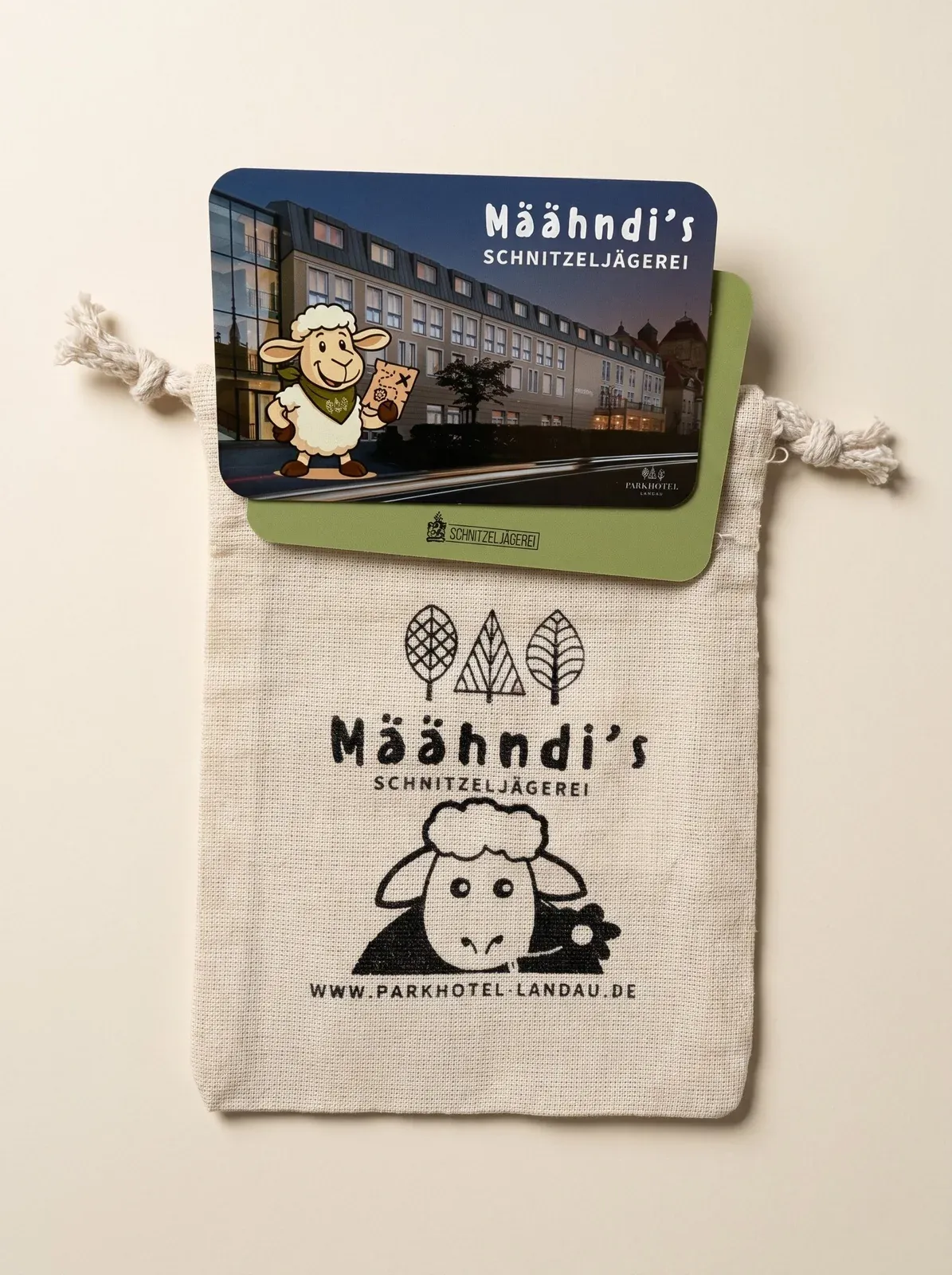 Gebrandetes Schnitzeljägerei-Kartenset für das Parkhotel Landau: Smartphone mit Maskottchen 'Määhndi' in der App, Bio-Baumwoll-Säckchen mit Maskottchen-Print und Karten mit Hotel-Illustration