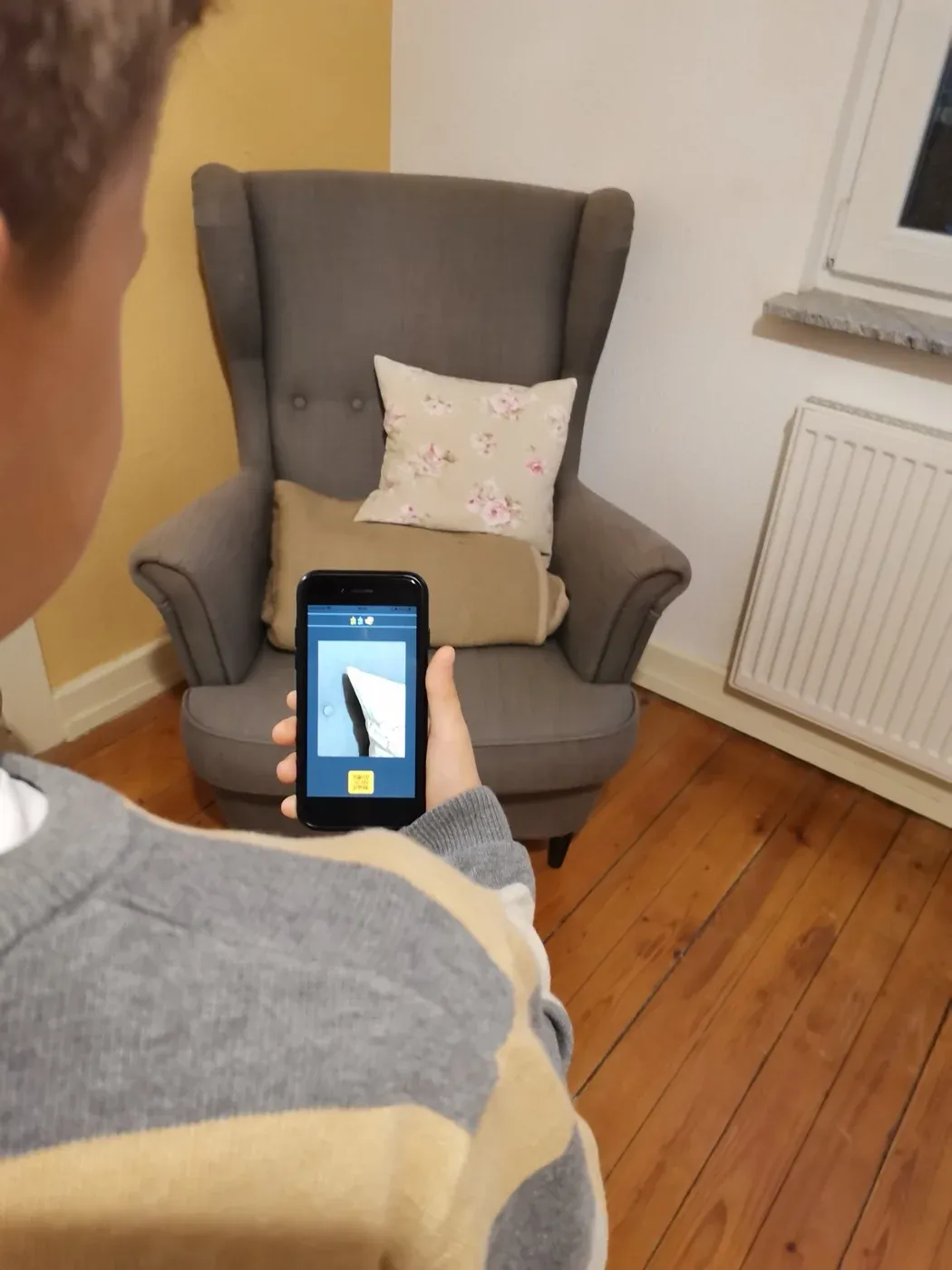 Kind hält ein Smartphone mit der Schnitzeljagd-App vor einen Sessel